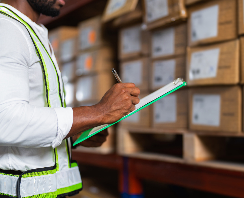 Side view of a man holding a clipboard checking inventory in a large distribution center