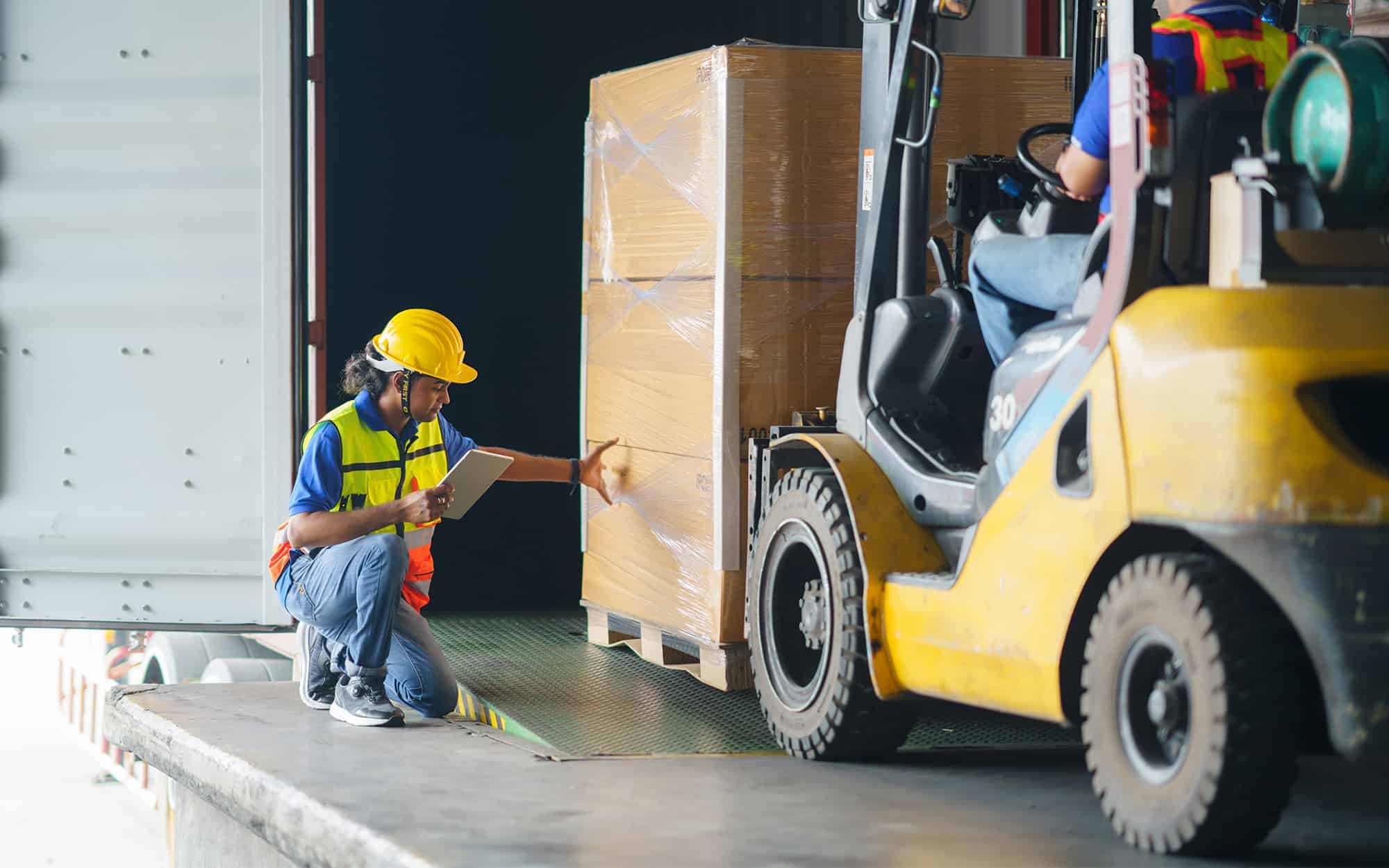 Side view of a warehouse worker touching boxes while they are on forklift