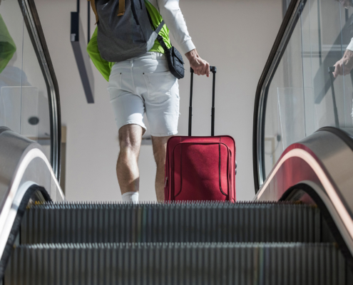 Male passenger with rolling travel luggage and backpack on a moving stairs escalator
