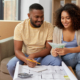 mortgage, moving and real estate concept - happy african american couple with blueprint and calculator counting money